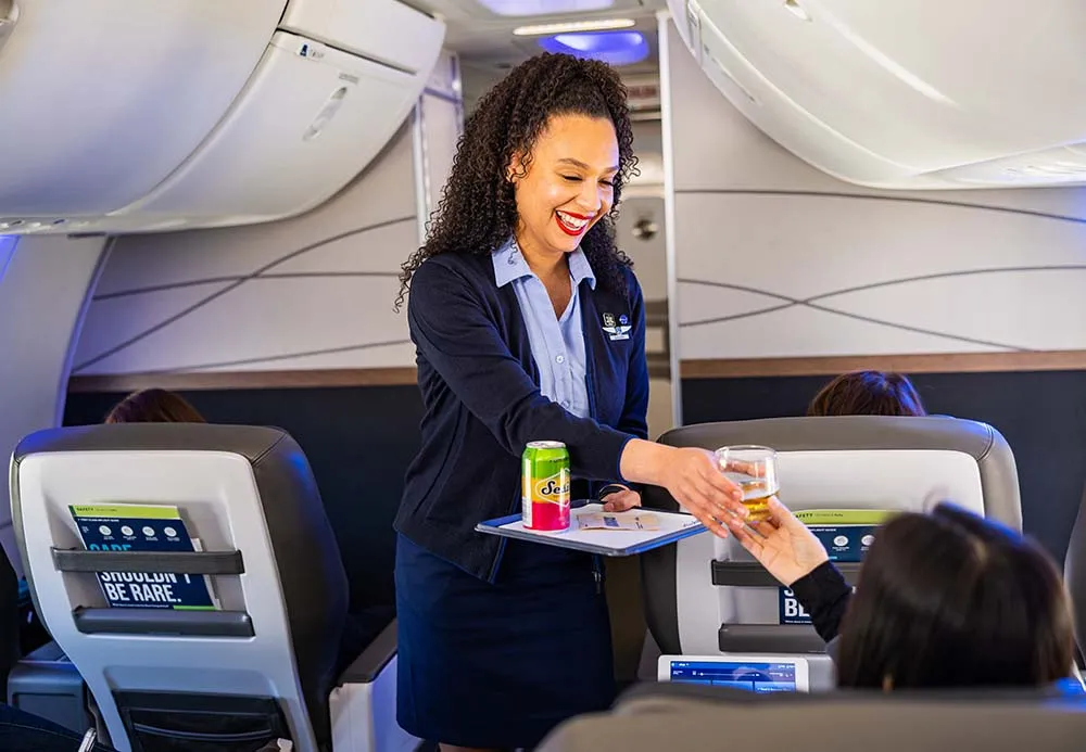 A flight attendant in uniform serves a drink to a seated passenger inside an airplane cabin.