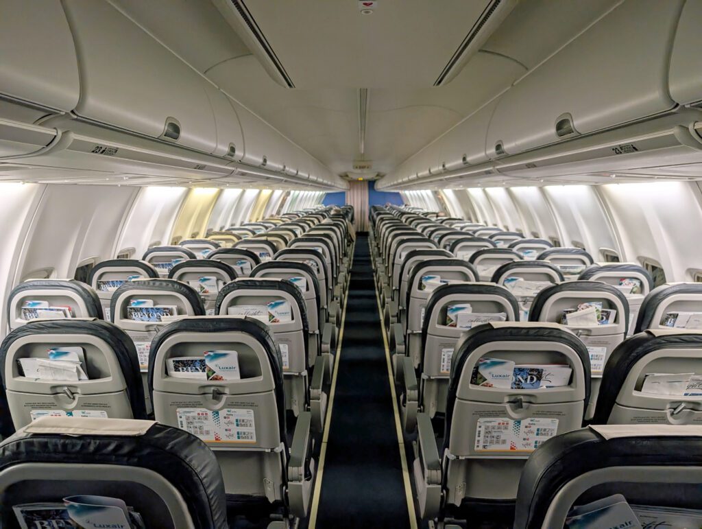 Innenraum eines Verkehrsflugzeugs mit Reihen leerer Sitze und Sitztaschen mit Sicherheitskarten und Zeitschriften, von hinten nach vorne gesehen.