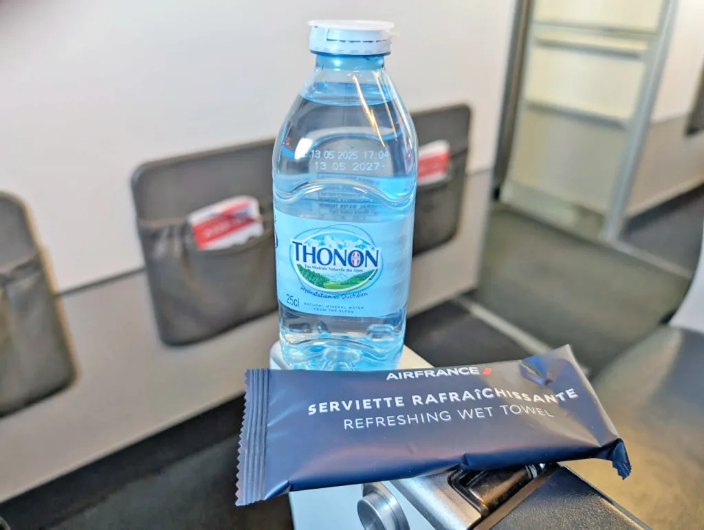 A bottle of Thonon water and a packaged Air France refreshing wet towel placed on an airplane tray table, reminiscent of the thoughtful amenities highlighted in many a Luxair review.