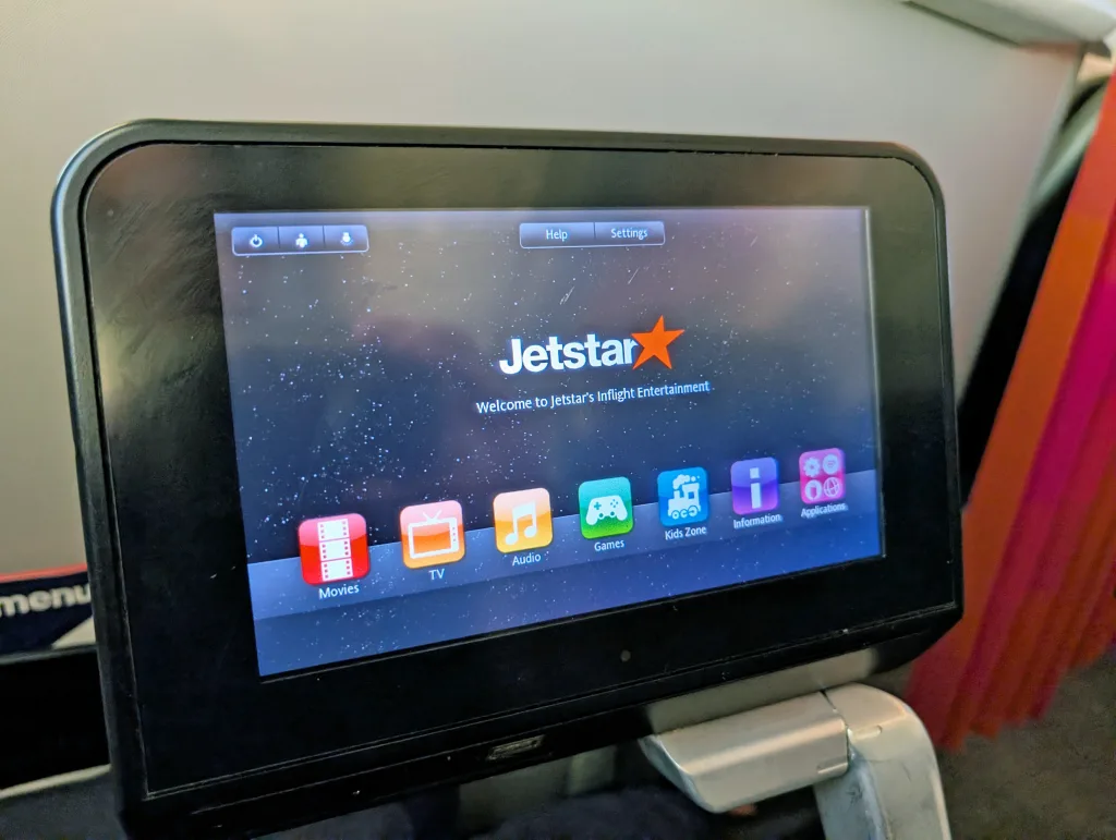 An in-flight entertainment screen on a Jetstar airplane displays options for movies, TV, audio, games, kids zone, information, and playlists.