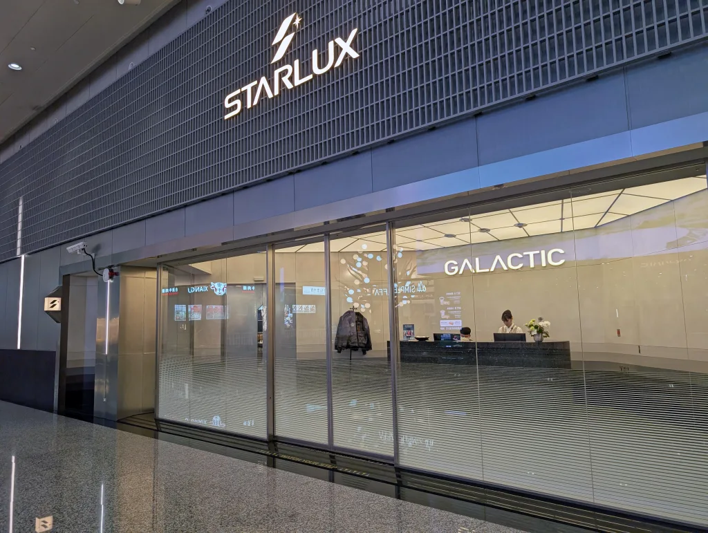 Glass entrance to the Starlux Galactic lounge with a reception desk inside and a staff member seated behind it.