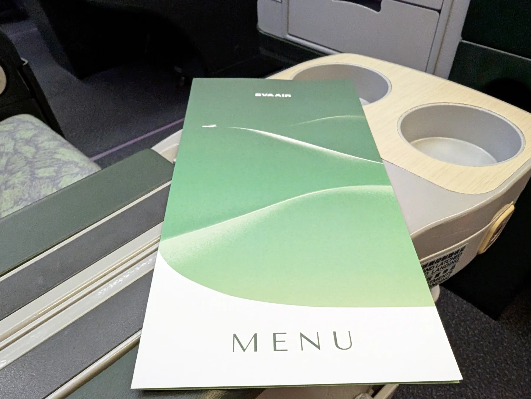 A green EVA Air menu rests on an aeroplane tray table next to cup holders.