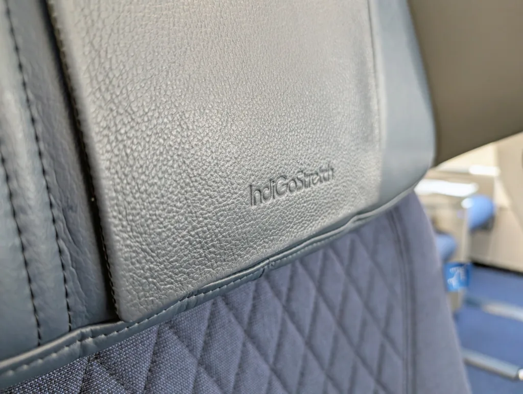 Close-up of an aeroplane seat with quilted dark blue fabric and a headrest cover embossed with the word "horizon.